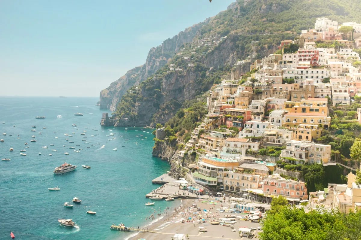 A picture of the Amalfi coastline with picturesque buildings on the hillside and many boats in the ocean.