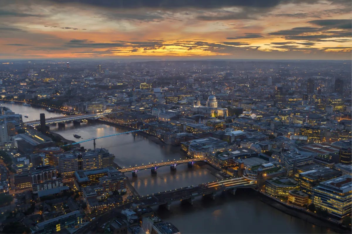 An aerial view of London at night with lights, a sunset and water.