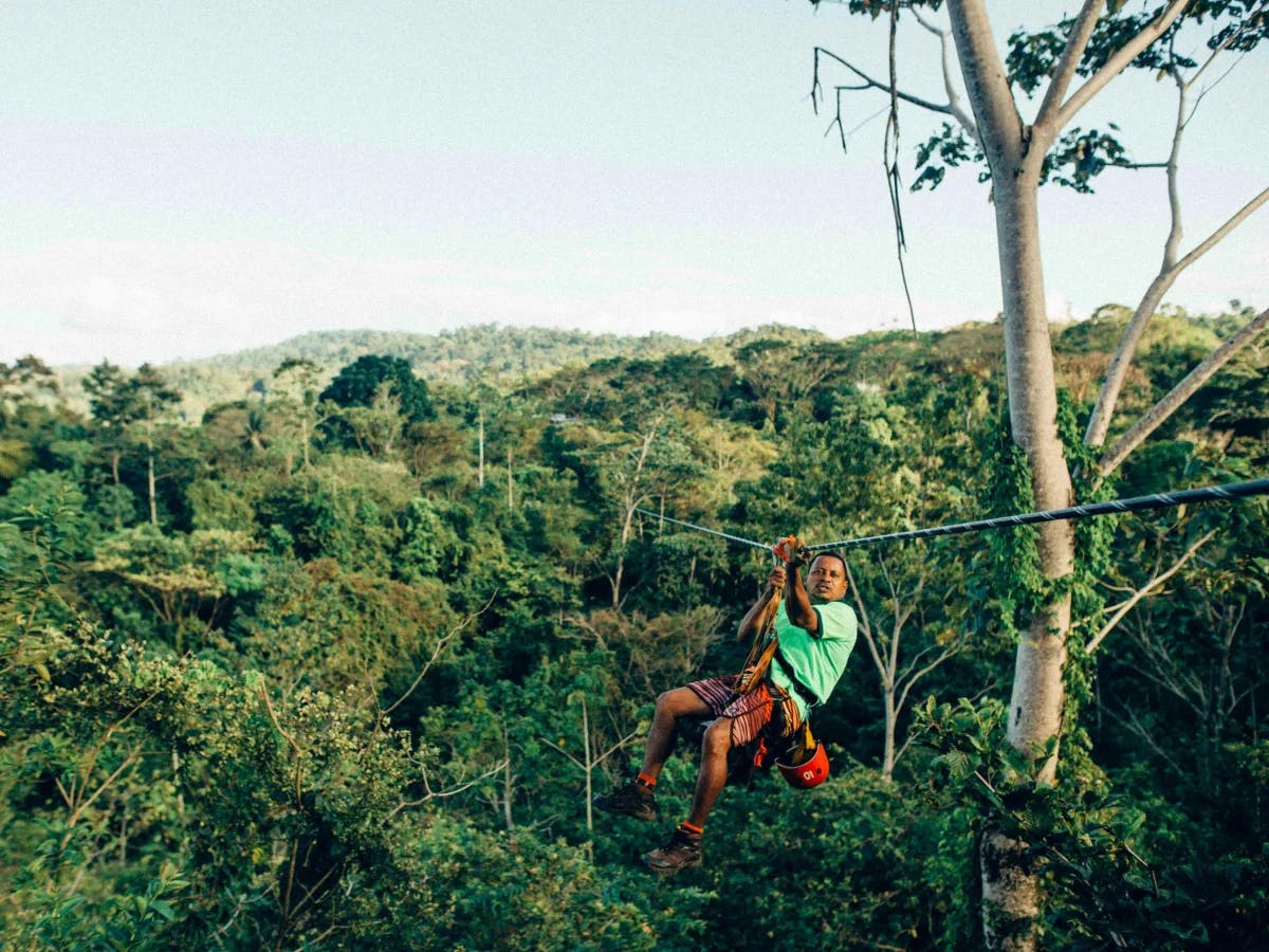 A picture of a person sliding on a zip line during the daytime.