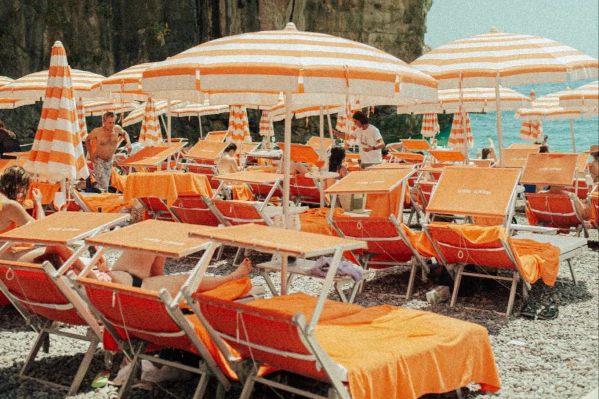 A view of orange and white striped umbrellas with chaise lounge chairs at Arienzo Beach Club during the day.