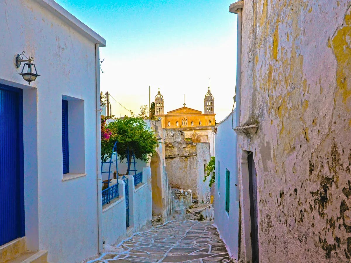 a-narrow-alley-way-with-a-clock-tower-in-the-background-paros-travel-guide