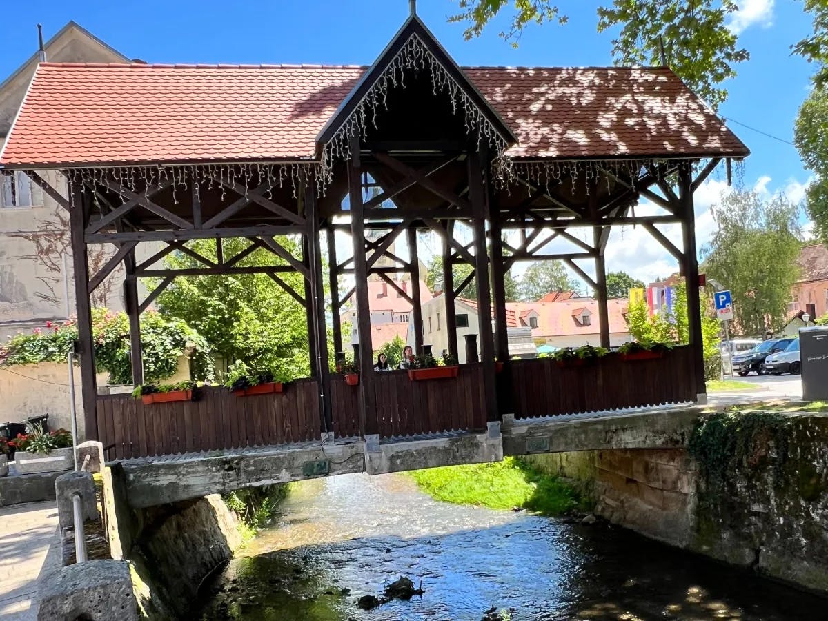 A view of an old bridge with red roofing, wooden paneling, and a creek beneath it. 