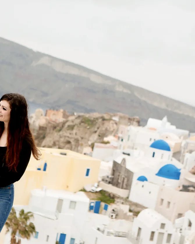 A woman in a black shirt and blue jeans standing on the seaside with a city view