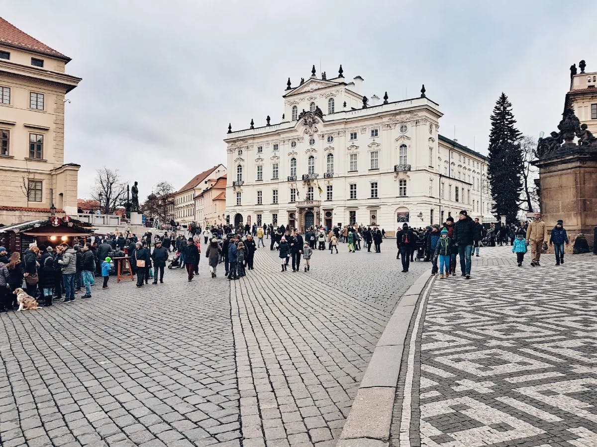 View of many pedestrians walking through a plaza on a cloudy day with a large white building visible in the center