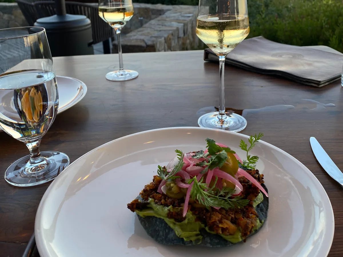 A salad on a white plate on a wooden table with glasses of wine