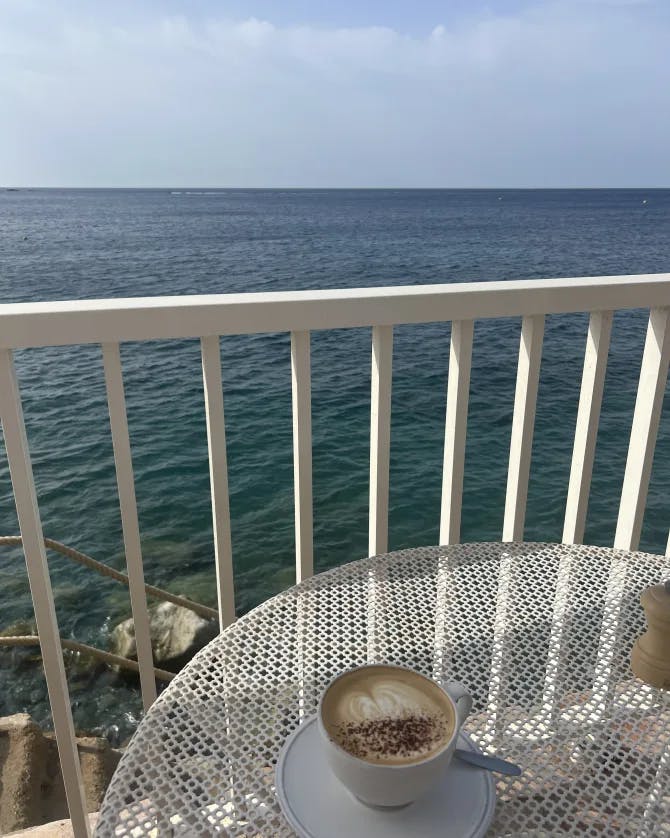 An outdoor table on balcony with a coffee and a view of the ocean in the distance. 