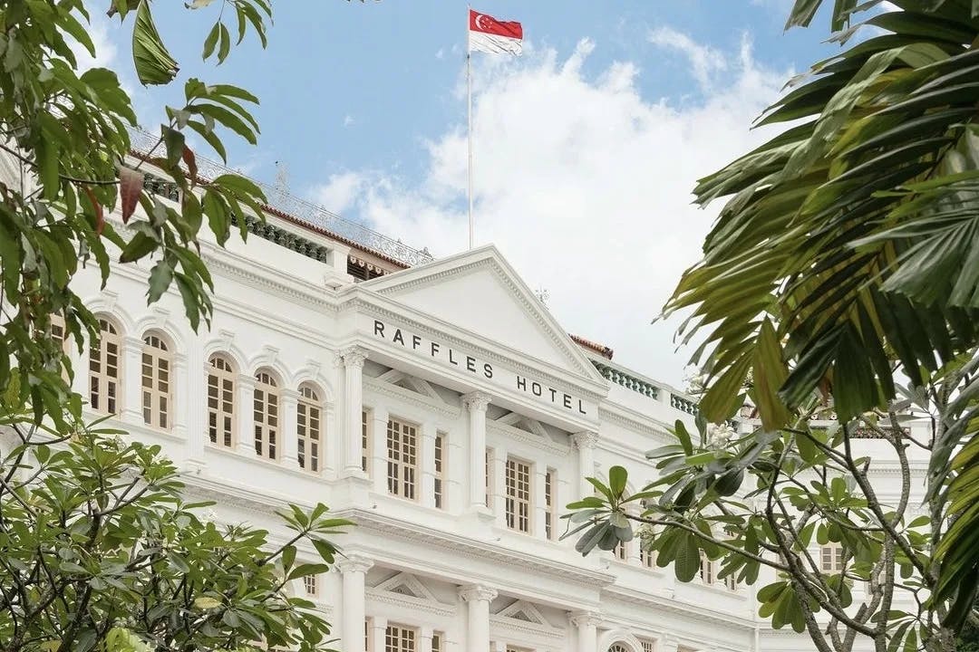 The exterior of a large white building with a sign reading "RAFFLES HOTEL" in black letters at the top