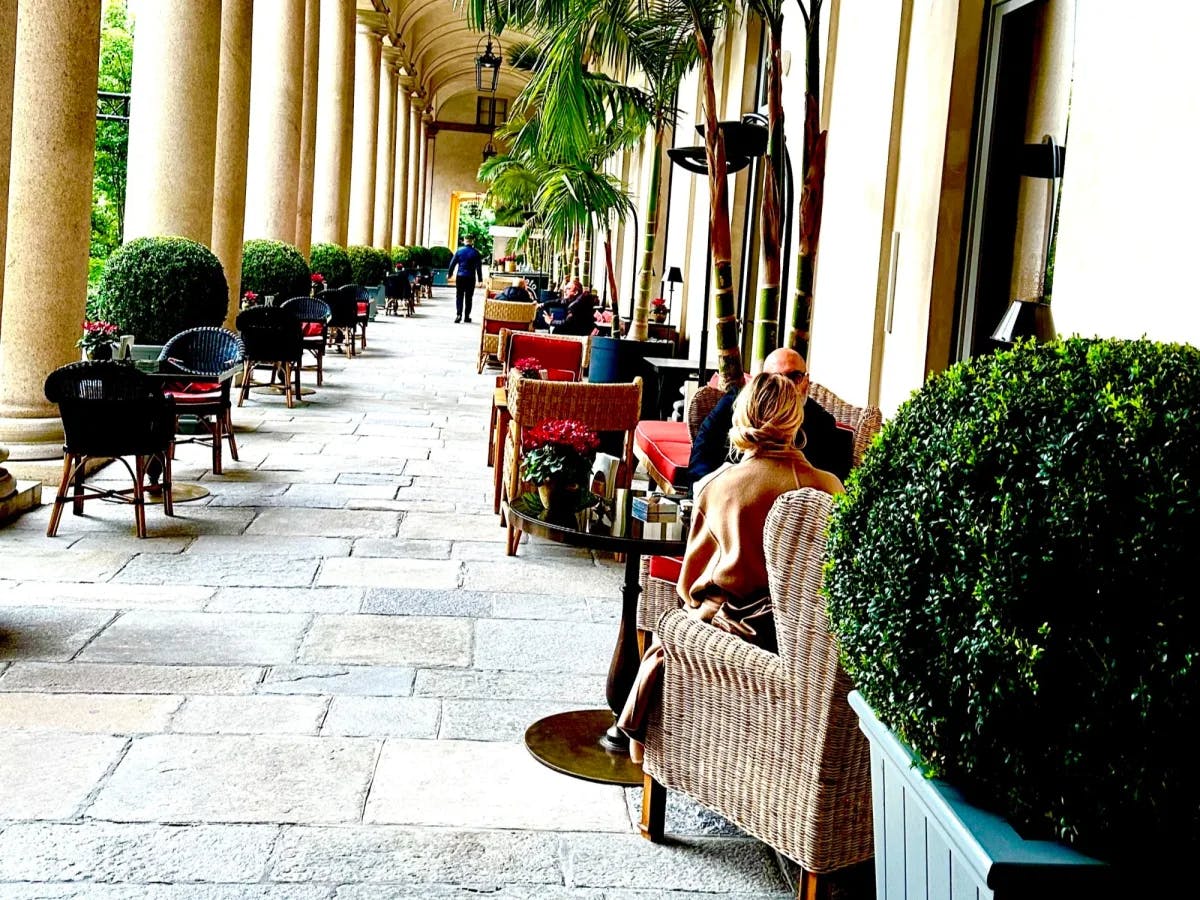 An outdoor hallway with people sitting at one side. 