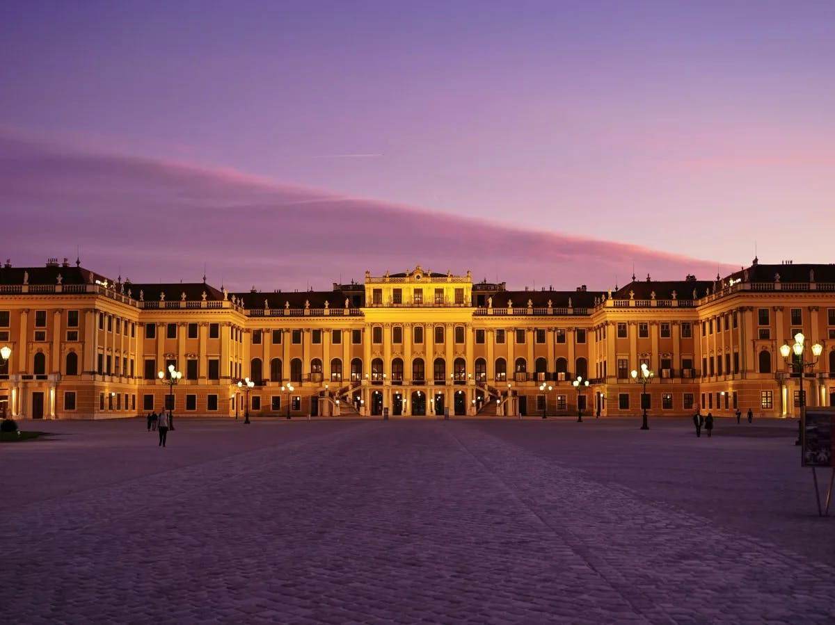 The grand Schönbrunn Palace illuminated at twilight with a spacious open square in the foreground.