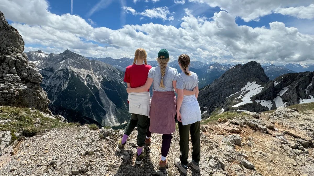 Three women looking over snow covered mountains. 