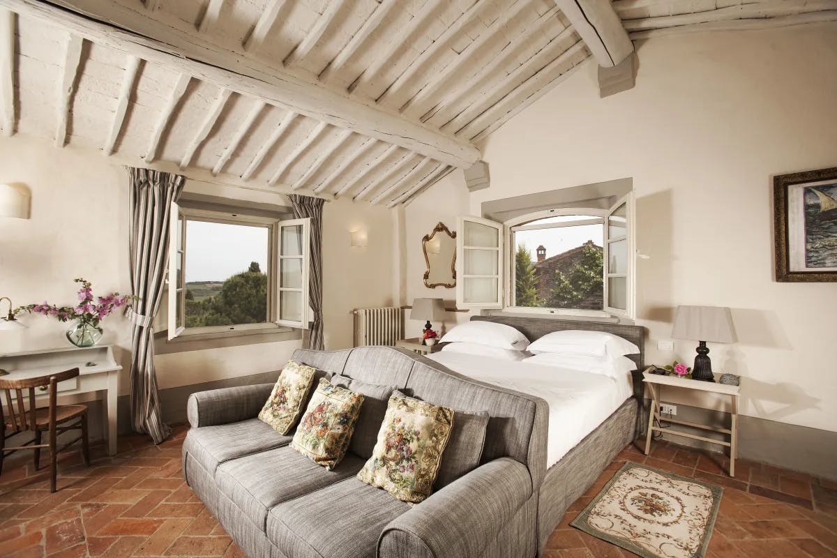 The Nido room with wood beam ceilings, stone floors, a white bed and Tuscan views out the windows