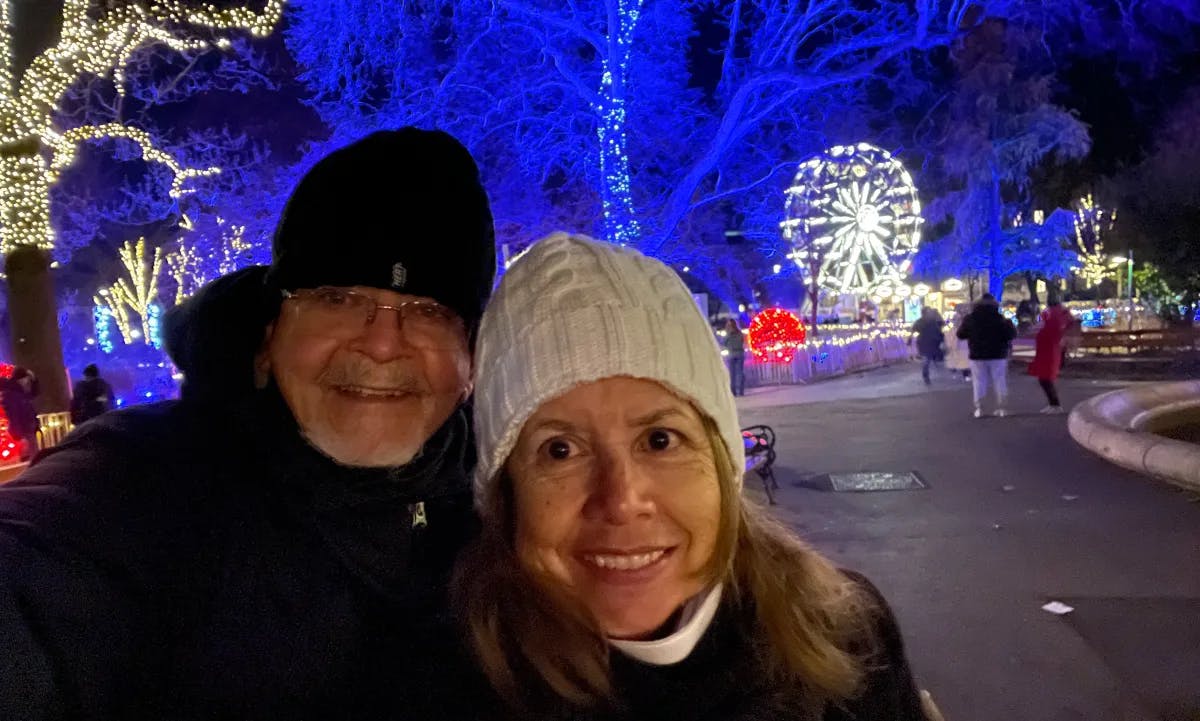 Advisor and her husband posing for a photo with blue Christmas lights in the distance at night.