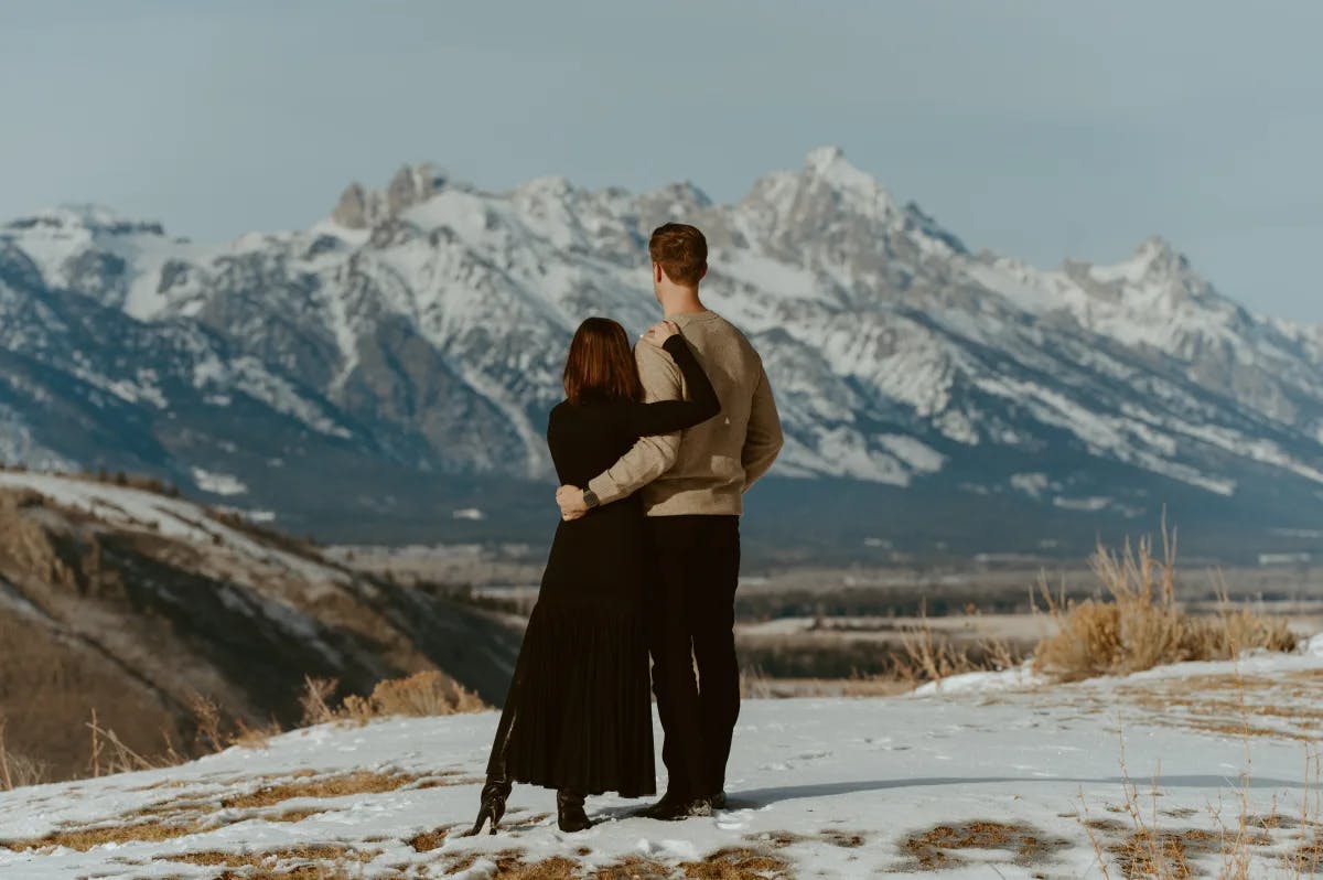 A couple with their back towards the camera, looking out onto the snowy mountains of Jackson Hole. 