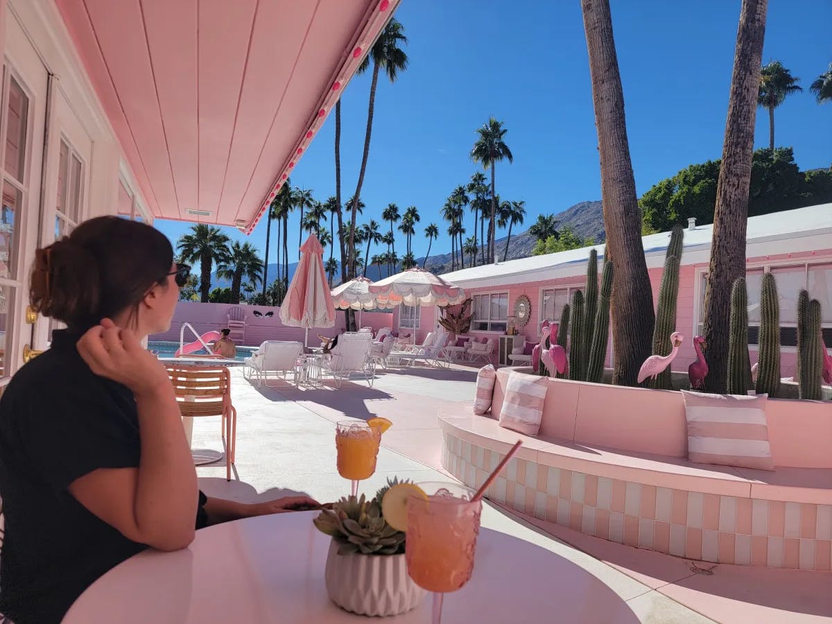 A woman sitting on a chair and table outside with drinks in front of her. 