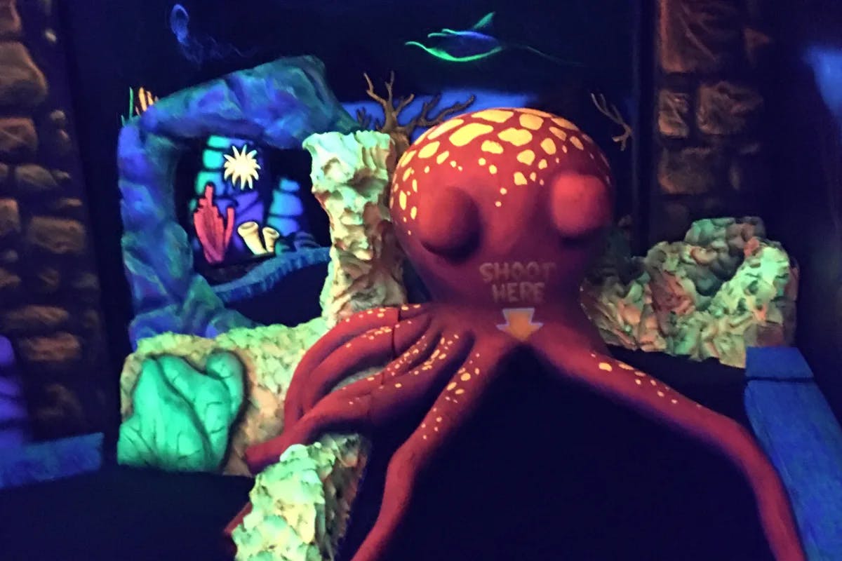 A Black Light Golf course with a large fake red octopus that says "shoot here" in front of a fake underwater background 