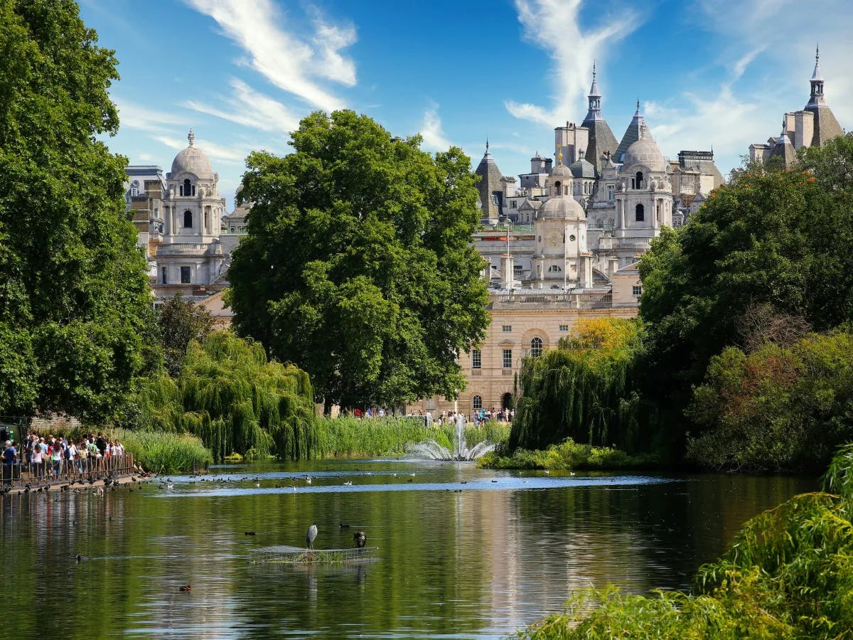 A grand historic building with intricate designs, set behind a serene pond and surrounded by lush greenery, exuding a peaceful atmosphere.