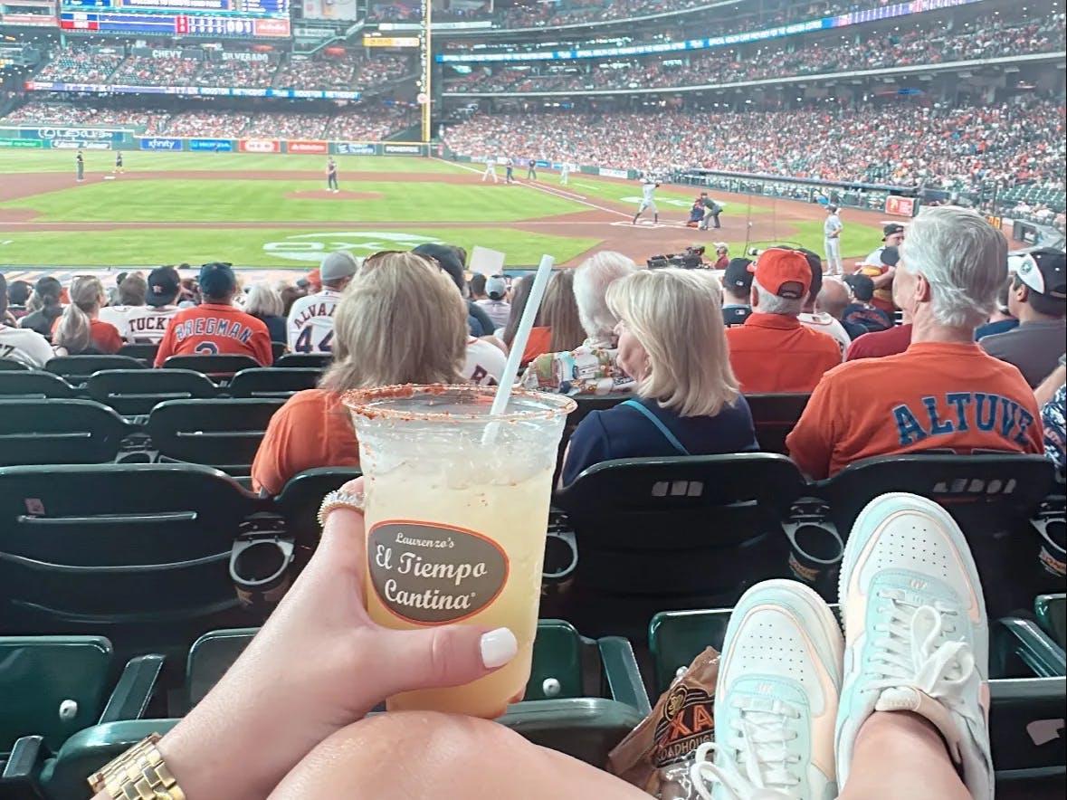 A picture of a person holding a drink at a stadium watching a game.