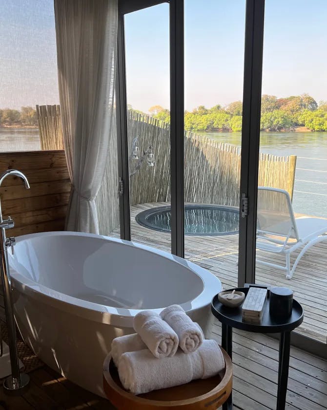 Picture of bathtub in a fancy hotel with an outside deck and nice chairs for relaxing that overlook a lake