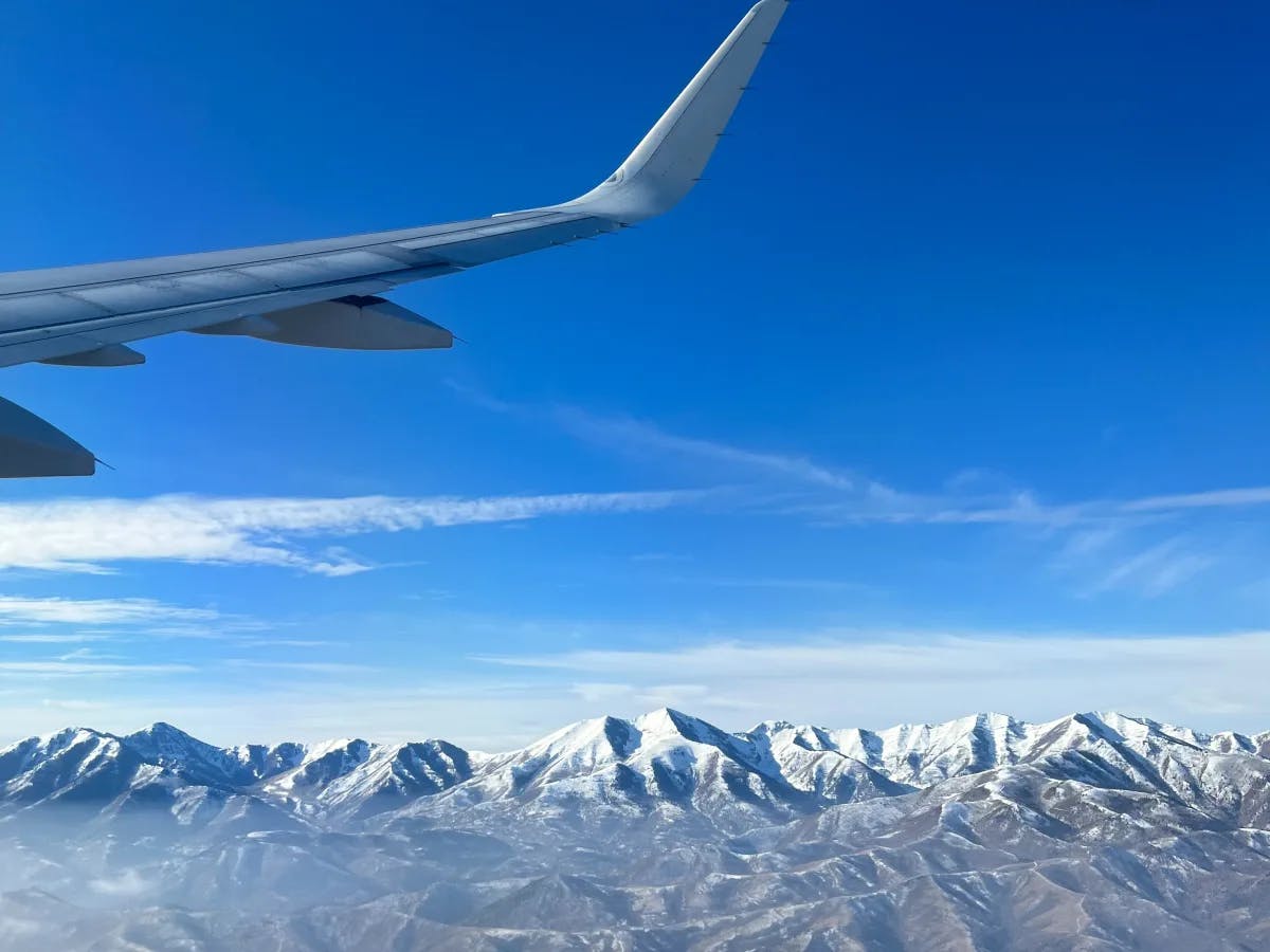 A view of an airplane wing flying over snow covered mountains.