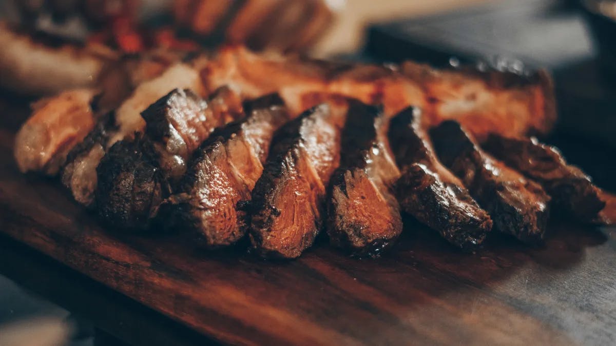 A wooden plate with strips of seared steak.