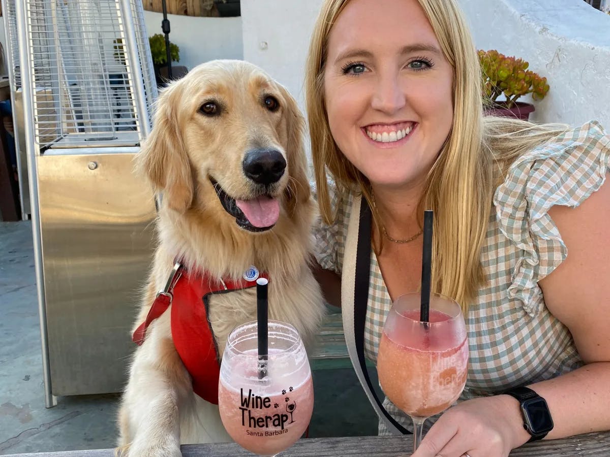 A woman posing with a Golden Retriever on an outdoor patio with frozen cocktails.