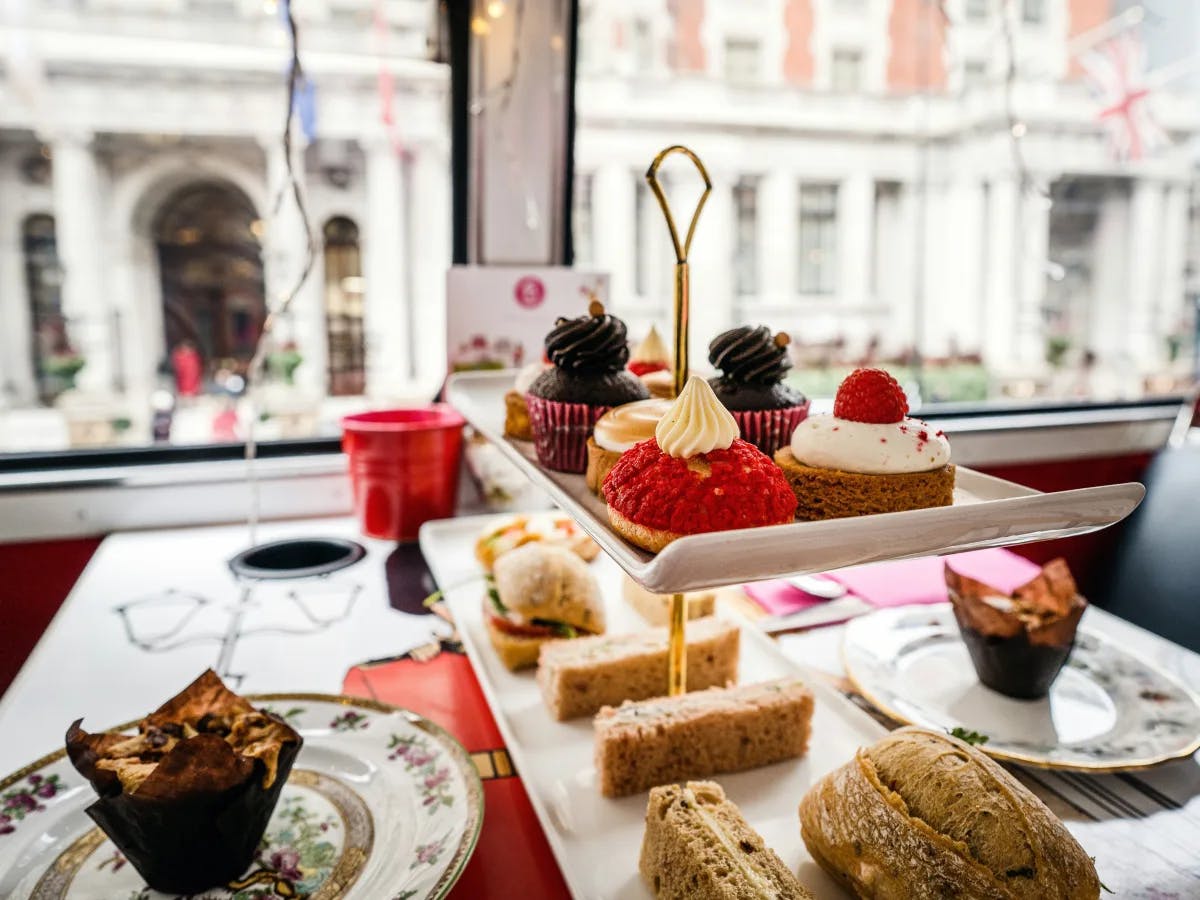 A delightful array of desserts and sandwiches on a tiered tray by a window with a street view.