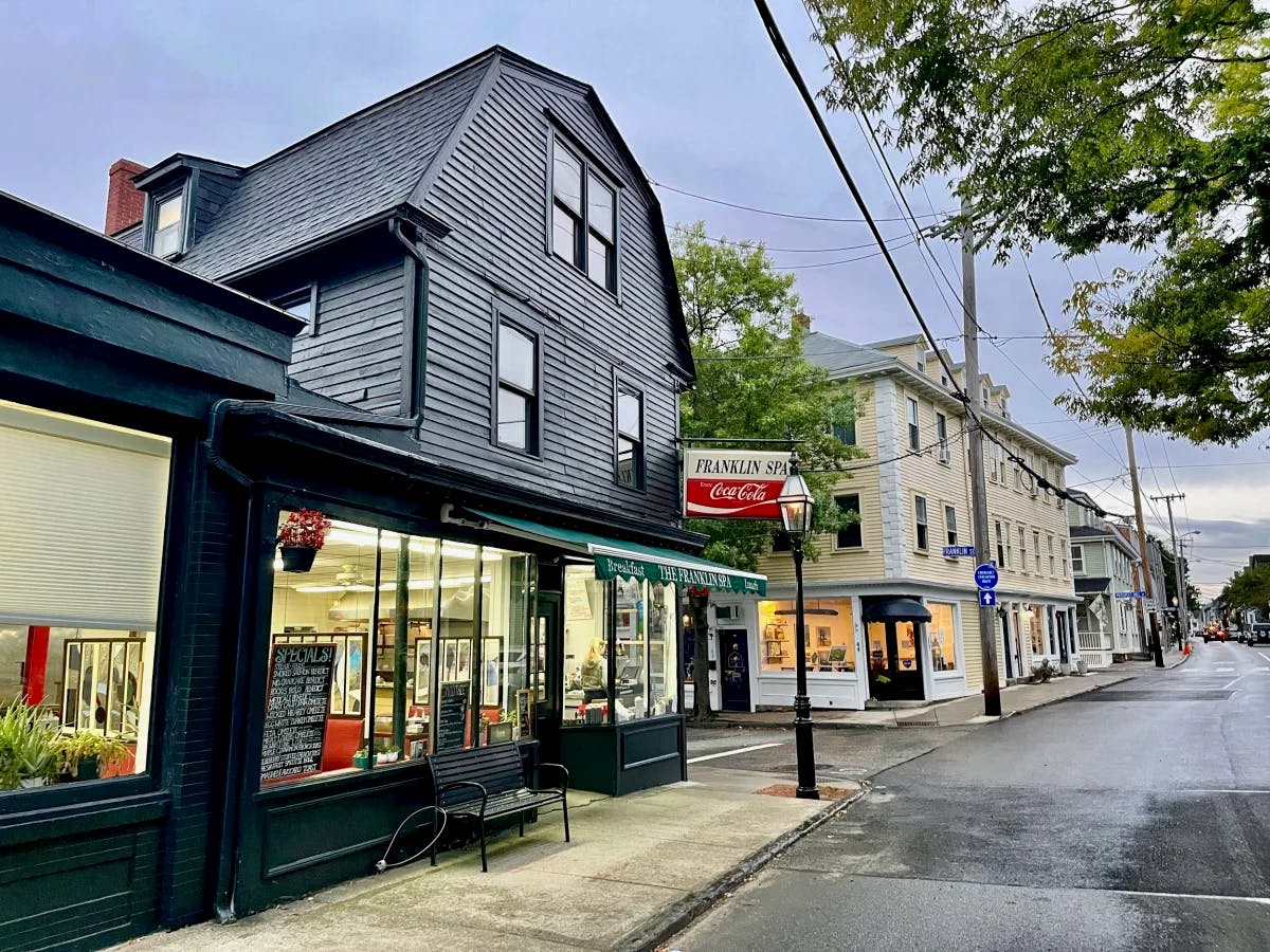 Franklin Spa in Newport, RI with a sign, black house and street with trees nearby. 