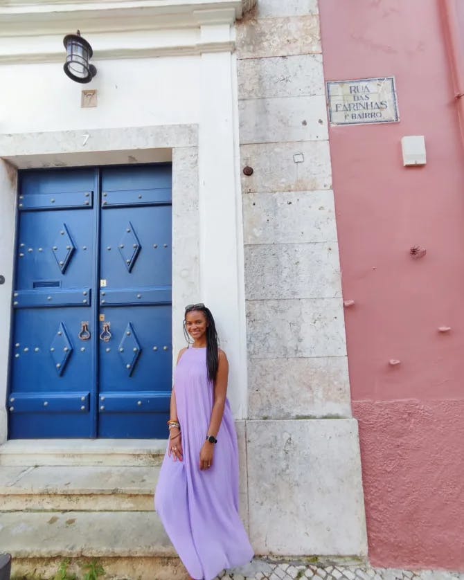 Colette in a long lavender dress leaning against a large stone doorframe with a blue door