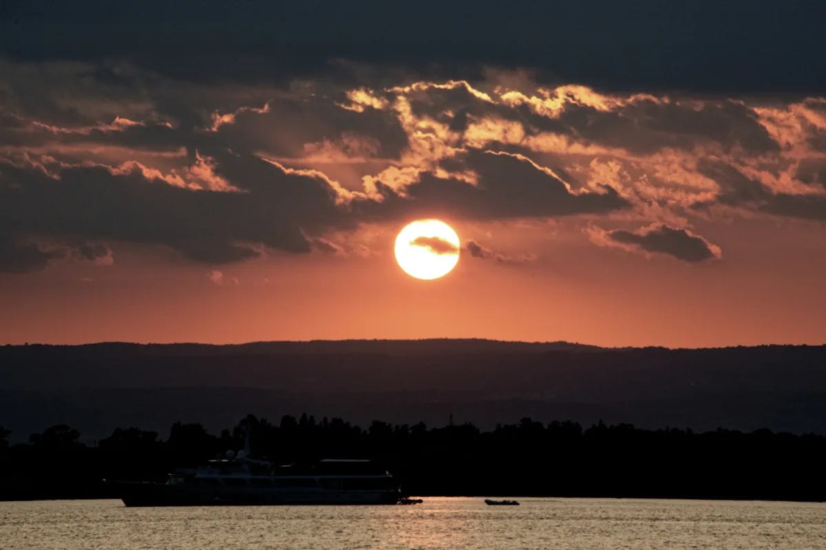 The sunset over the ocean, with the silhouette of mountains and grey clouds.