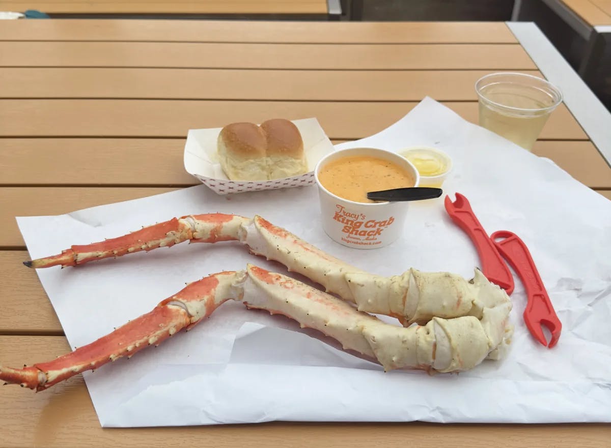 A crab leg on a picnic table with a cup of soup and plate of bread.