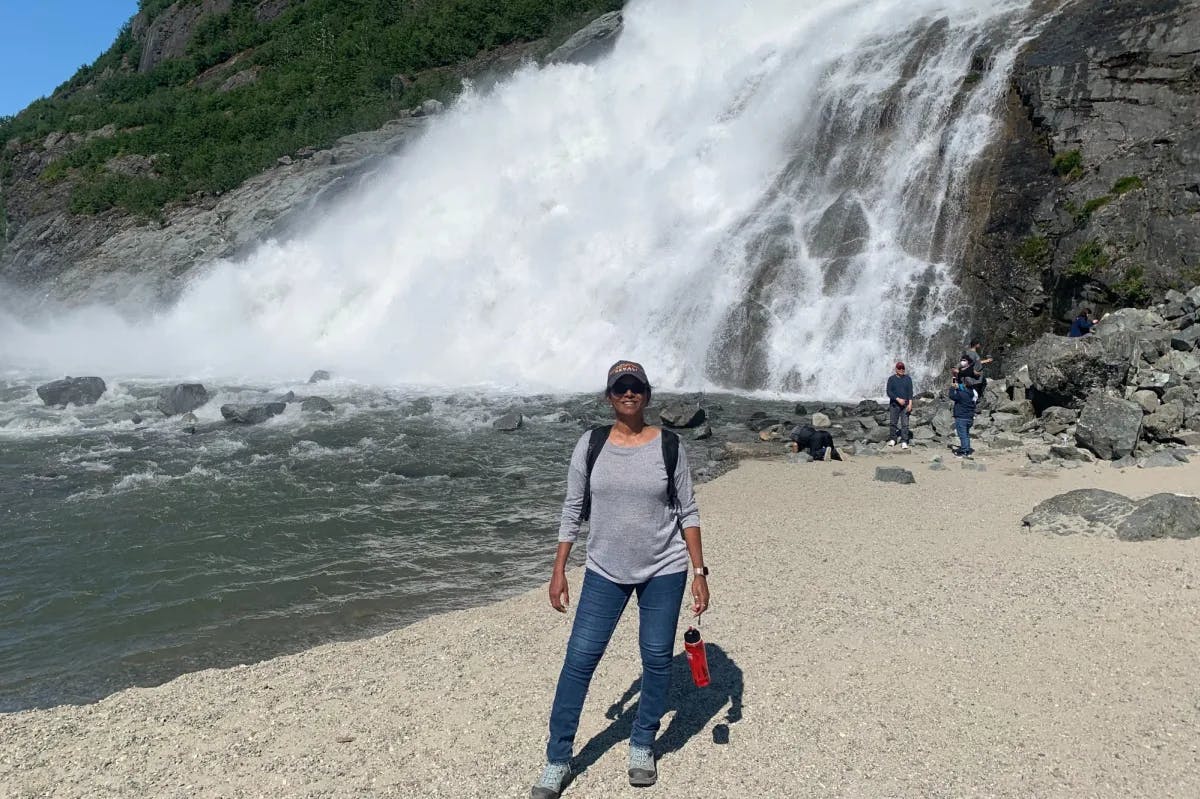 woman standing on pebble beach with waterfall behind