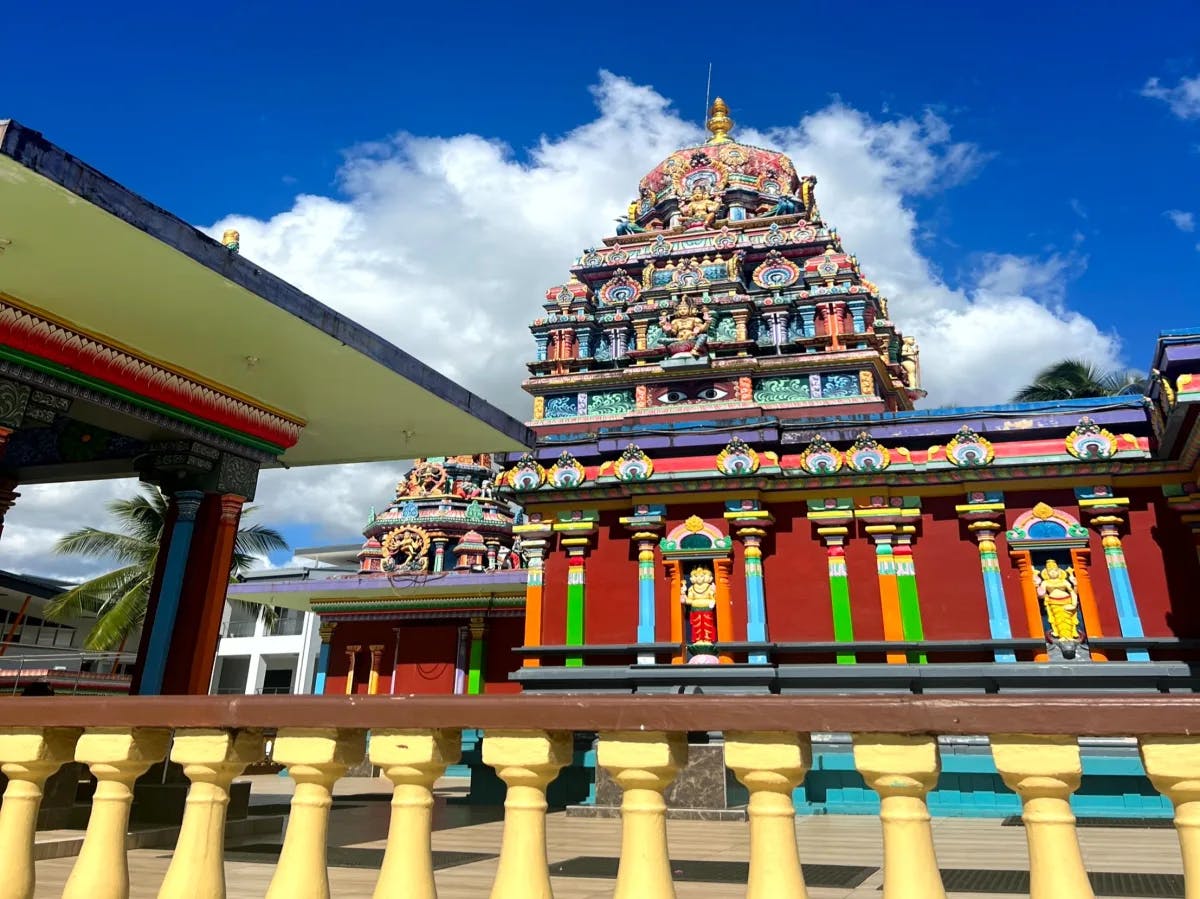 A vibrantly colored, multi-tiered temple under a clear blue sky with fluffy clouds.