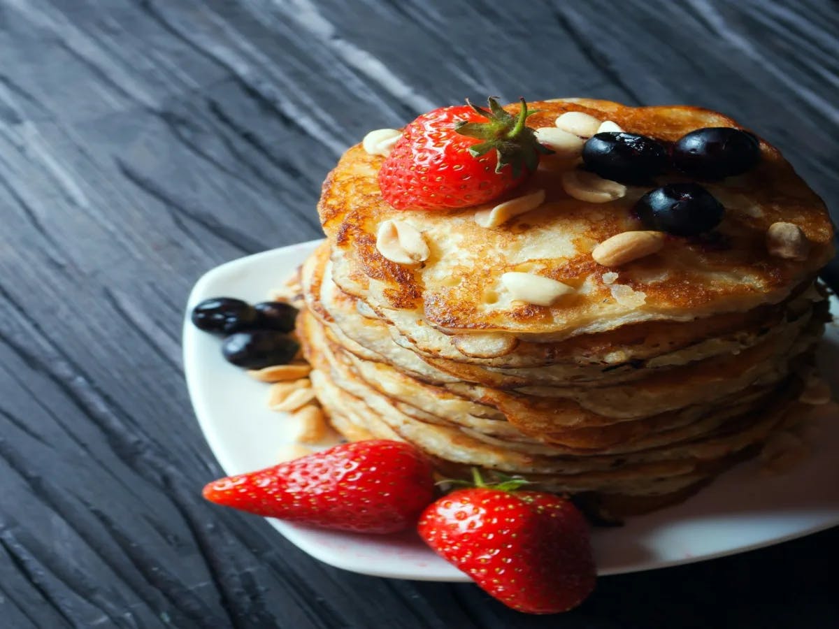 A stack of pancakes topped with strawberries, blueberries, and nuts sits on a plate with additional strawberries beside it.