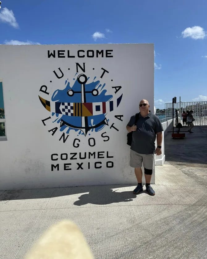 Advisor standing by a wall with a welcome to Cozumel, Mexico under sunny skies