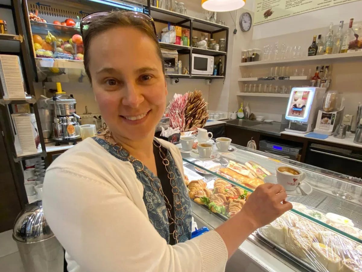 An individual is serving food at a deli counter, with a variety of items on display and menu boards in the background. 