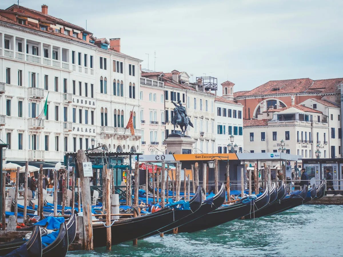 A picture of the buildings near the water with boats lined up during the daytime.