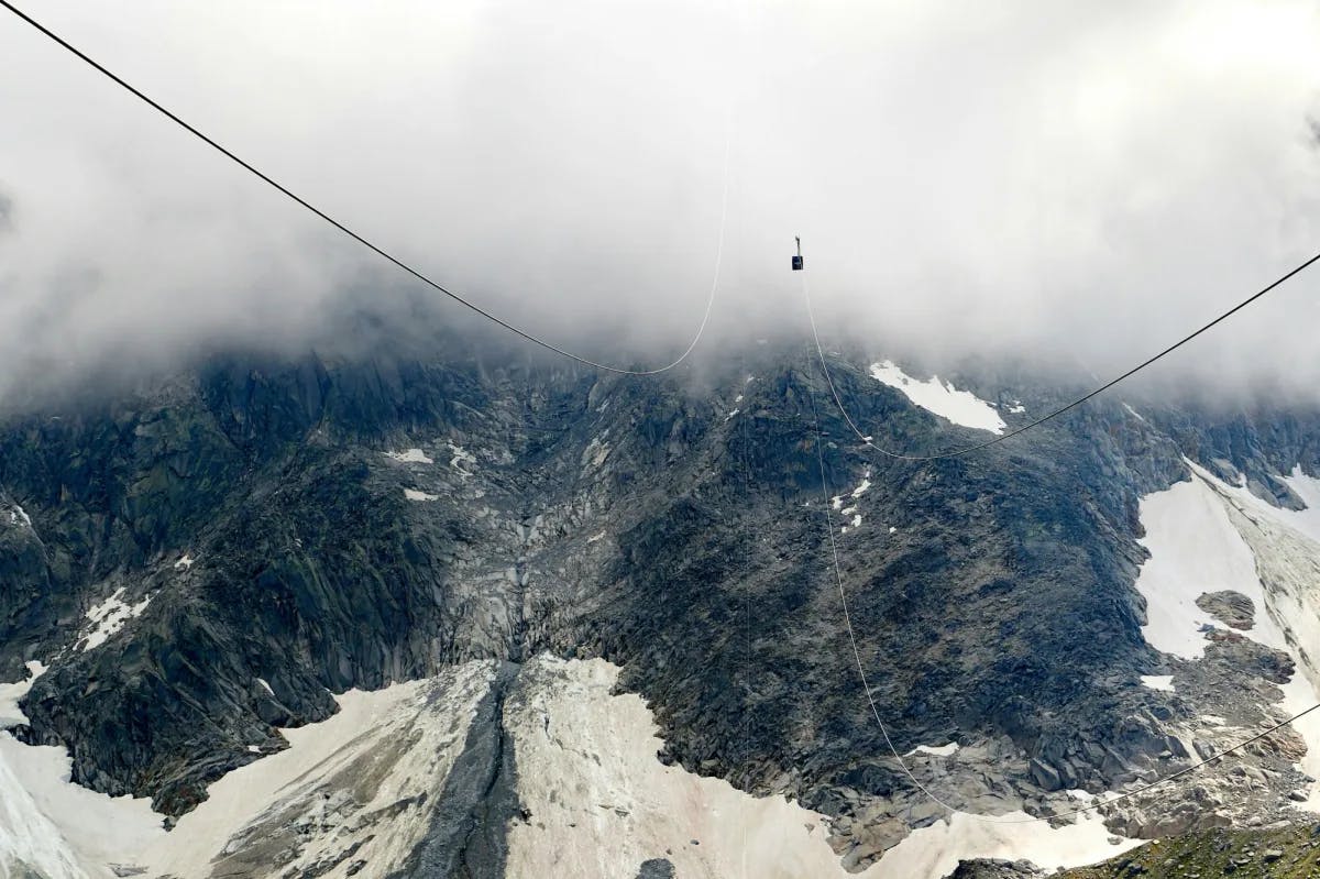 A view of cable car lines looking downward onto snowy mountain terrain and thick fog.