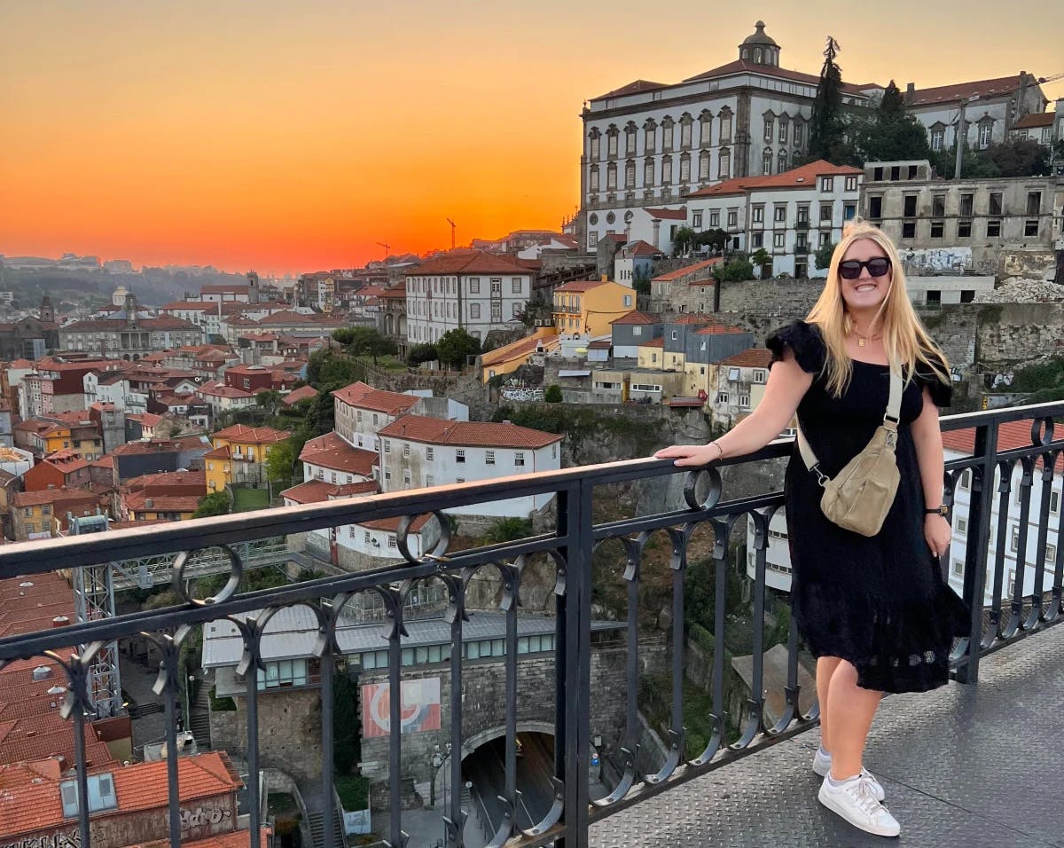 Alyssa in a black dress on a bridge overlooking the city of Porto at sunset.