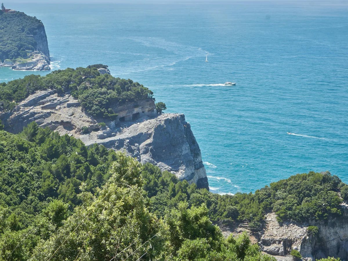 The image portrays a serene coastal landscape with a white sailboat, where lush greenery meets the calm blue sea.