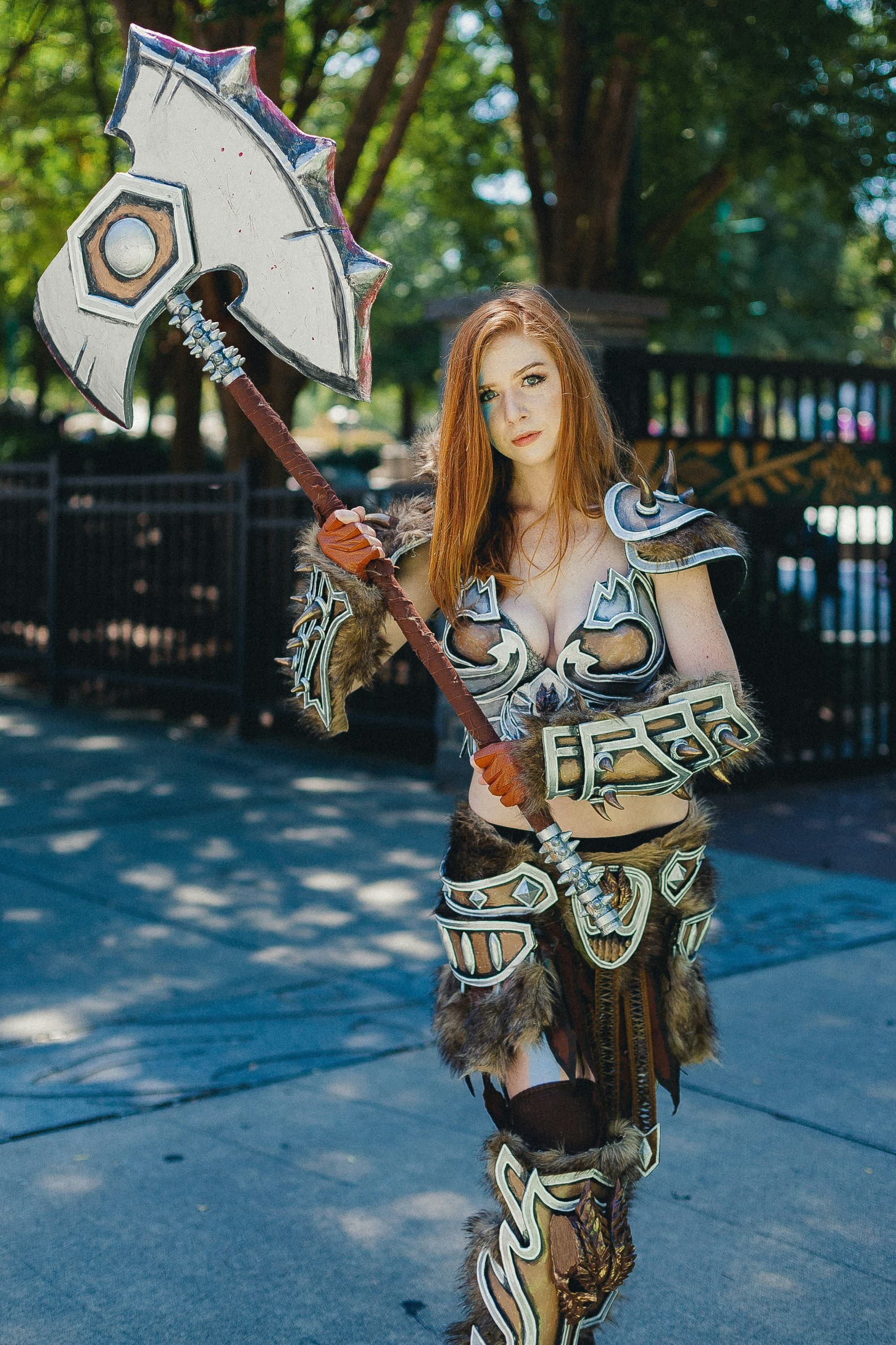 The image shows an individual in detailed cosplay armor with a large axe, standing outdoors.