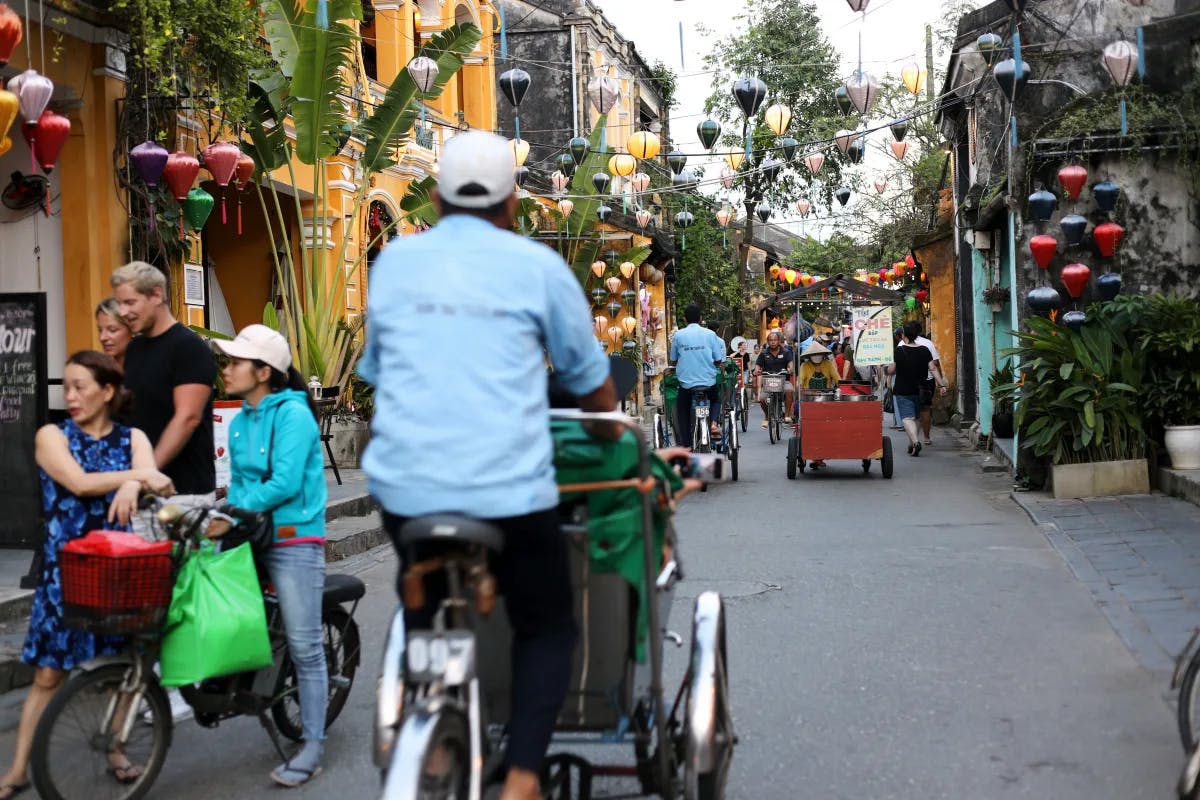 A quaint pedestrian street in Hanoi with people cycling and lanterns hanging from the stores.