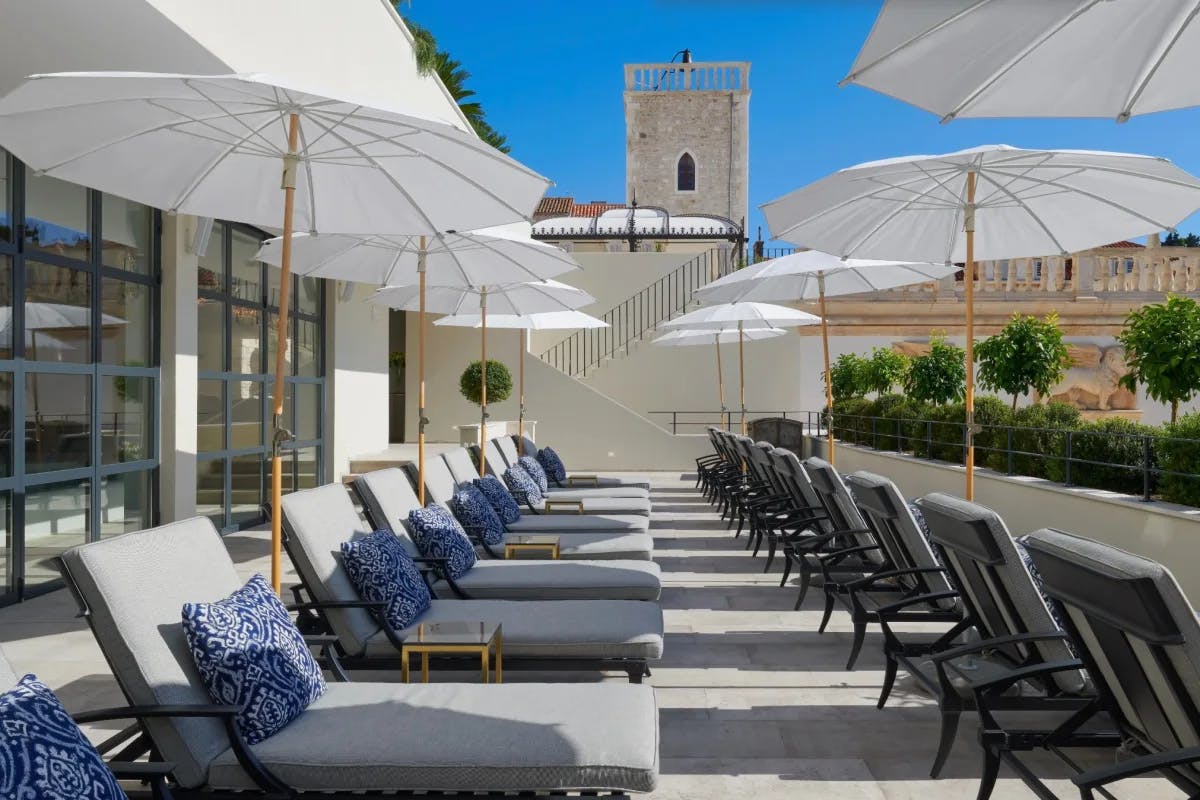 rows of cushioned loungers with blue pillows and white umbrellas and blue sky