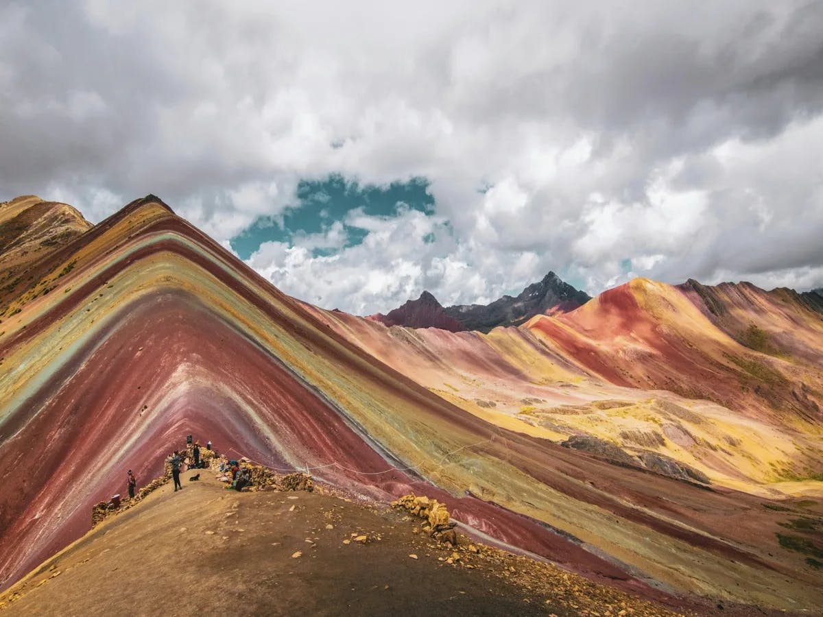 A vibrant tapestry of Rainbow Mountain’s multicolored strata unfolds under a dramatic sky.