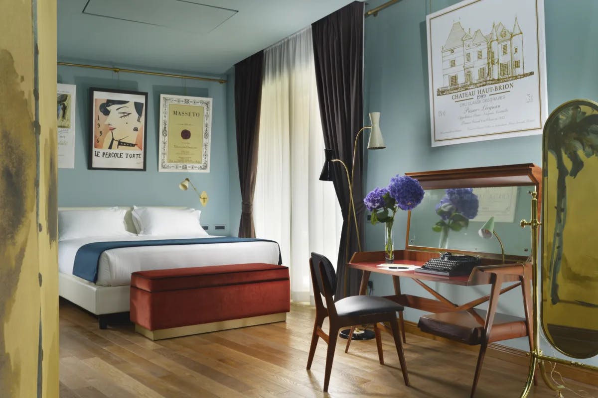 a hotel bedroom with teal walls and a desk on which rests a vase of purple flowers