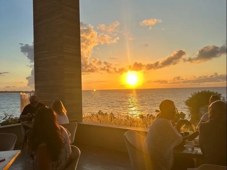 People sitting at an outdoor restaurant with a view of the sunset over the ocean