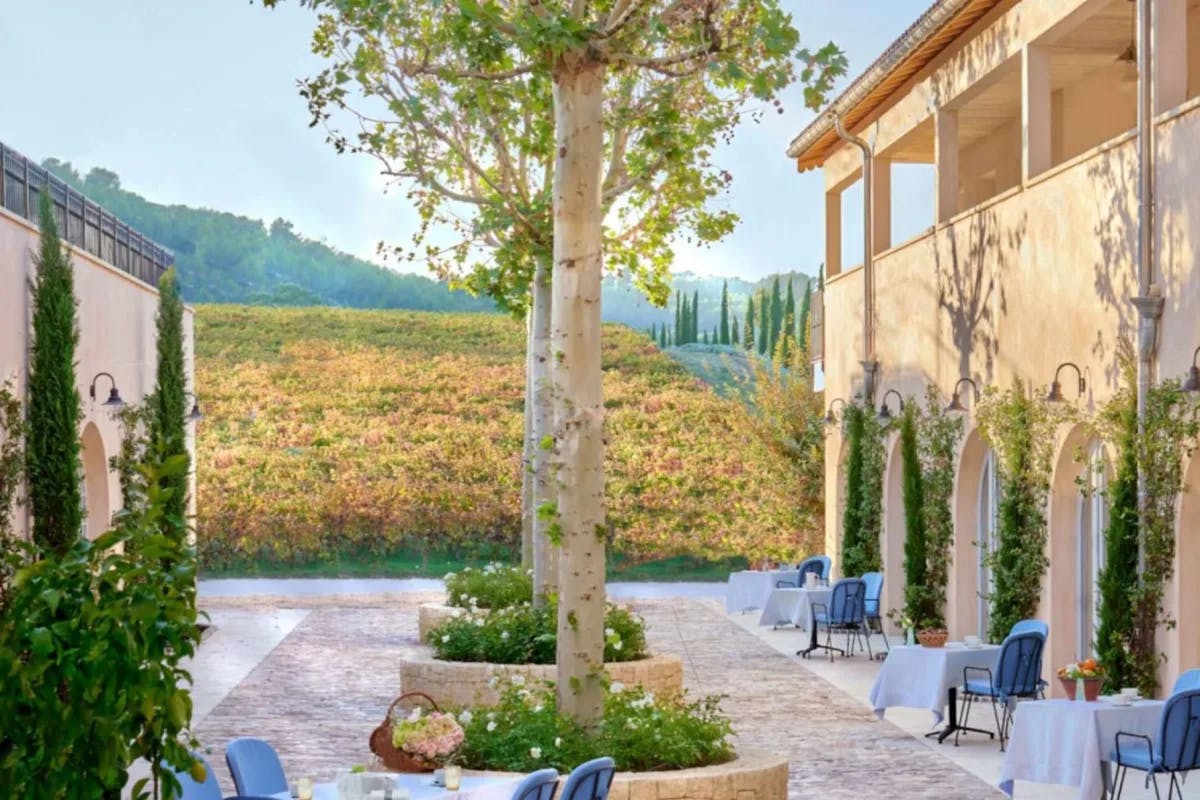 stone courtyard with dining tables and tree in the middle and fields and hills beyond