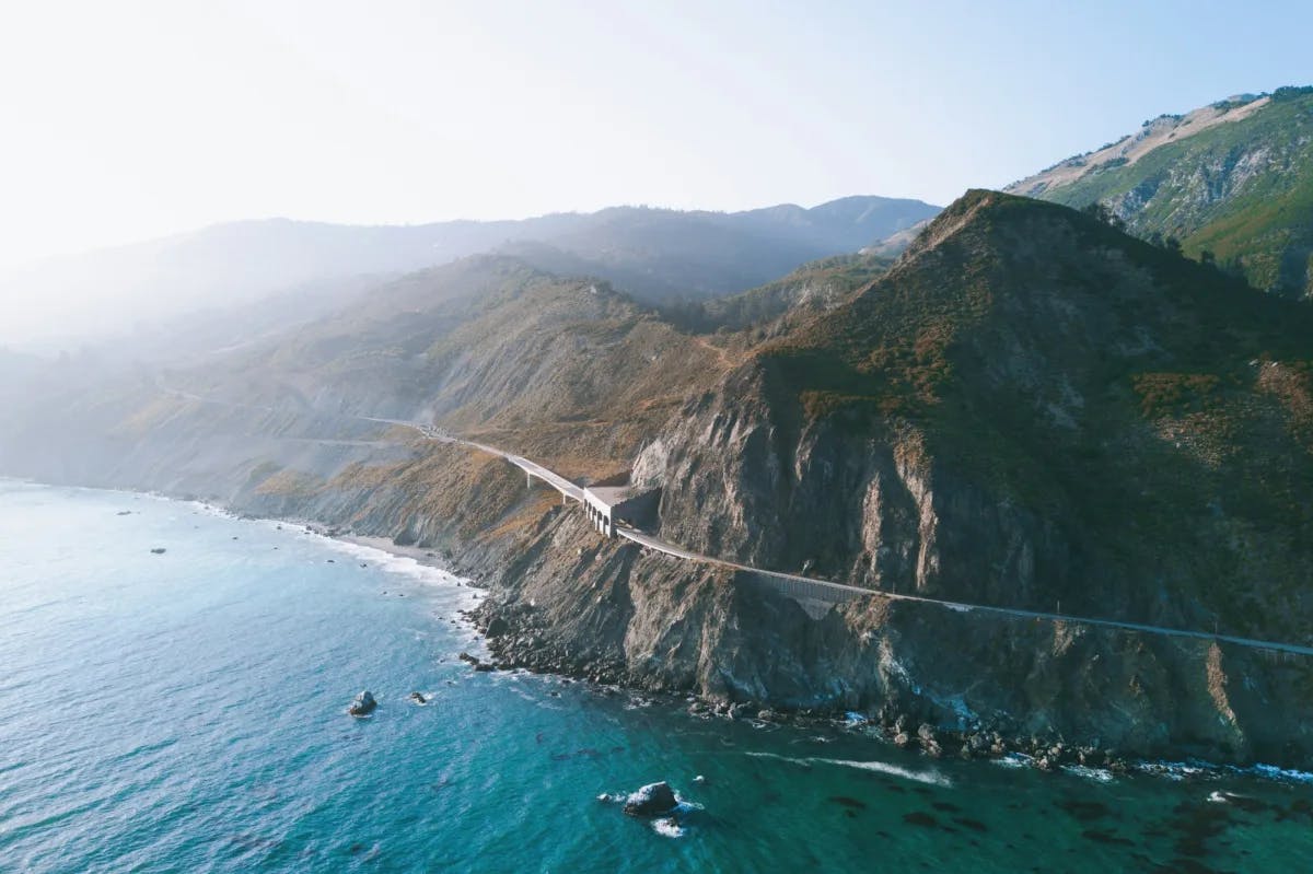 blue ocean with mountains and a road heading into a tunnel