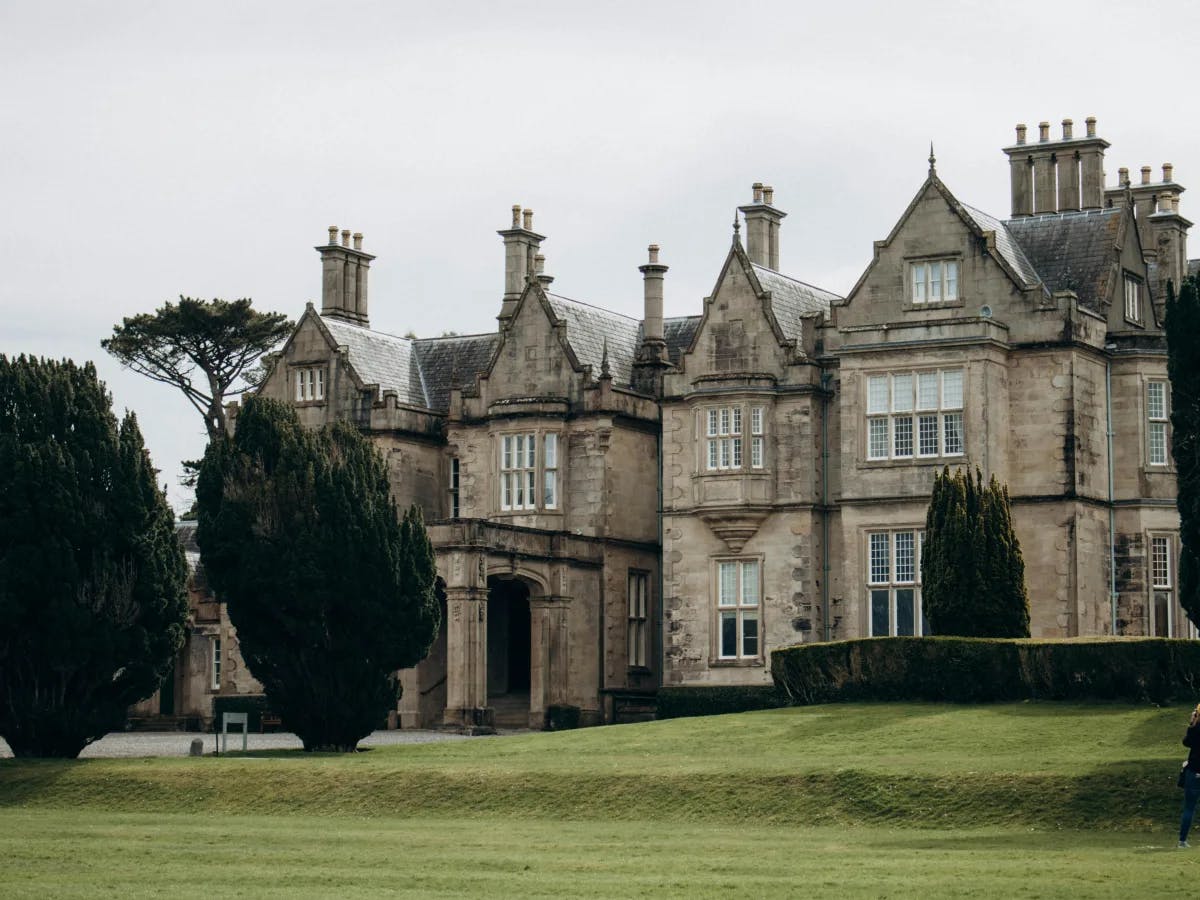 A grand, old mansion with multiple chimneys and bay windows, set against an overcast sky.