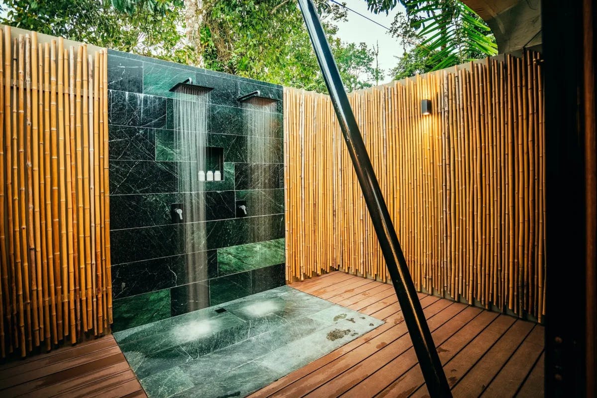 A spacious outdoor shower with twin rain spouts, bamboo-lined walls and no ceiling, revealing the Costa Rican rainforest