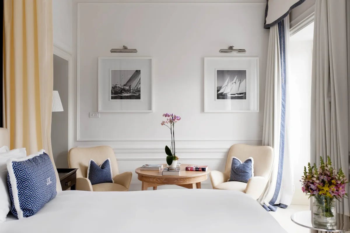 a white bed in a breezy, posh bedroom with cream-colored chairs